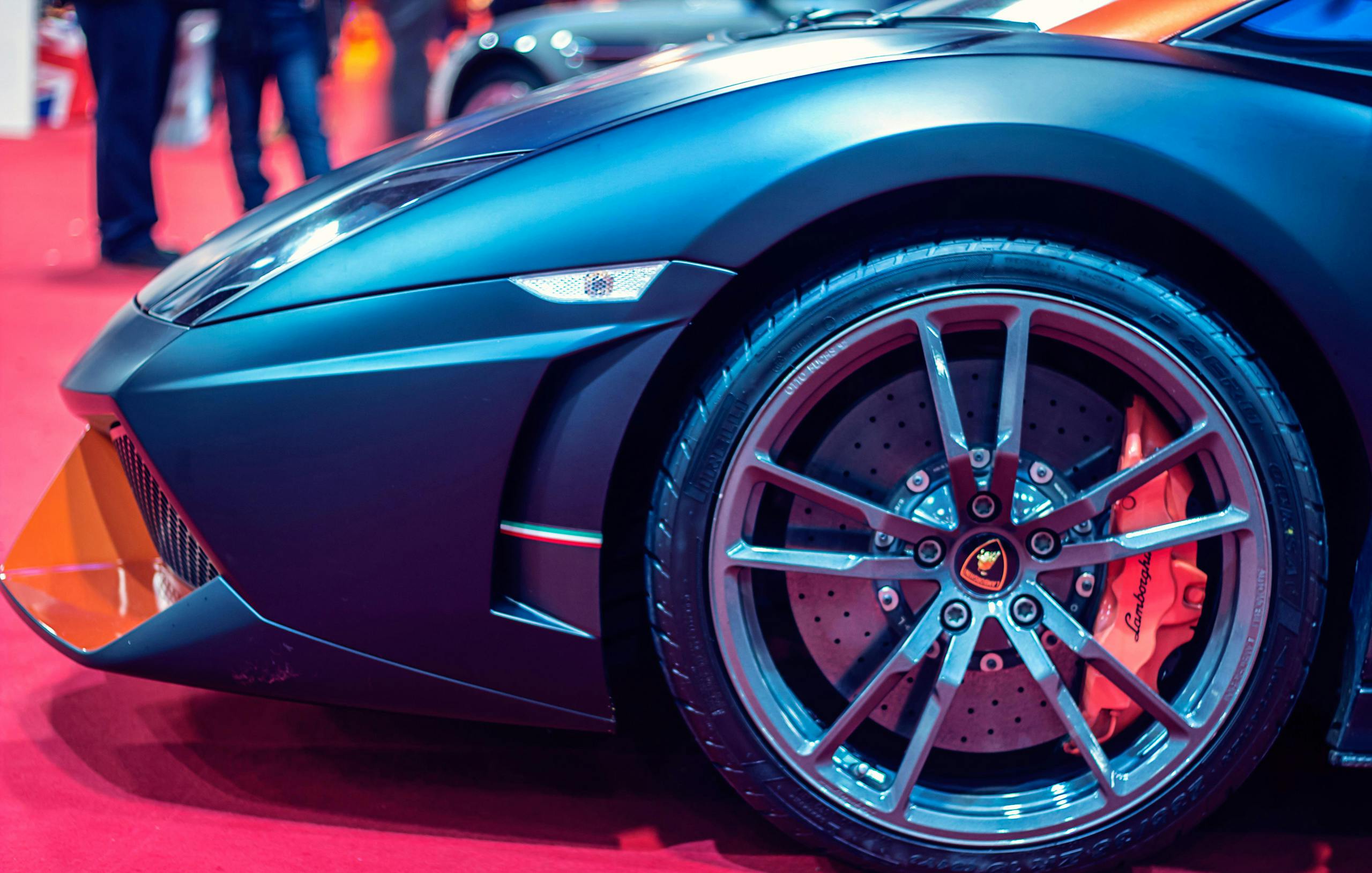 Close-up of a matte black Lamborghini showcasing its sleek design, featuring a distinctive wheel with a vibrant orange brake caliper.